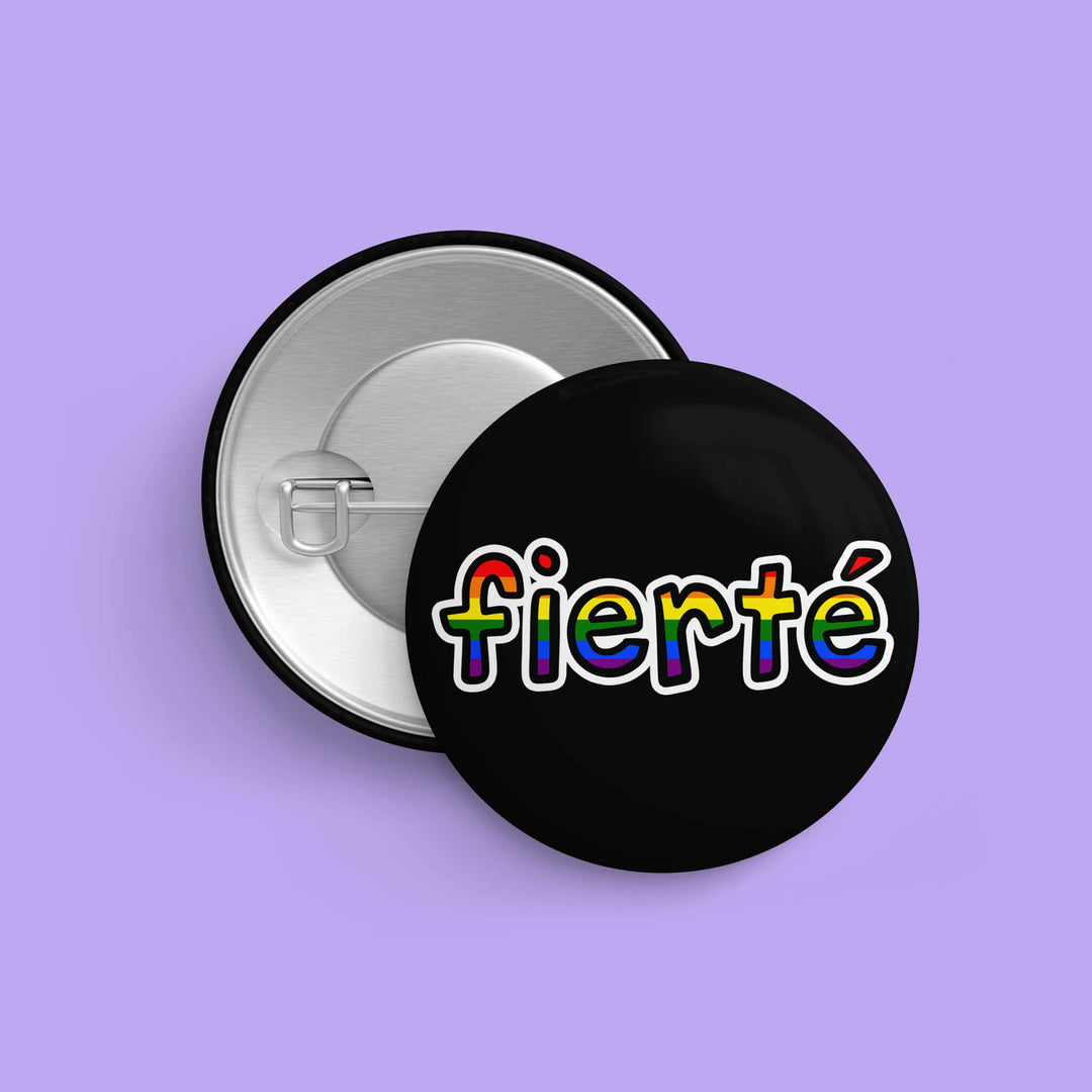 LGBTQIA+ Button « Fierté » mit Regenbogen-Schriftzug sowie Rückseite mit Sicherheitsnadel auf lila Hintergrund, Durchmesser 32 mm.