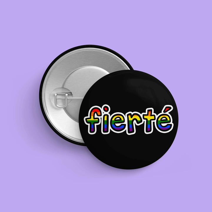 LGBTQIA+ Button « Fierté » mit Regenbogen-Schriftzug sowie Rückseite mit Sicherheitsnadel auf lila Hintergrund, Durchmesser 32 mm.