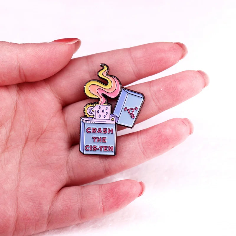 Emaille-Pin „Crash The Cis Tem“ in einer Hand gehalten zum Größenvergleich