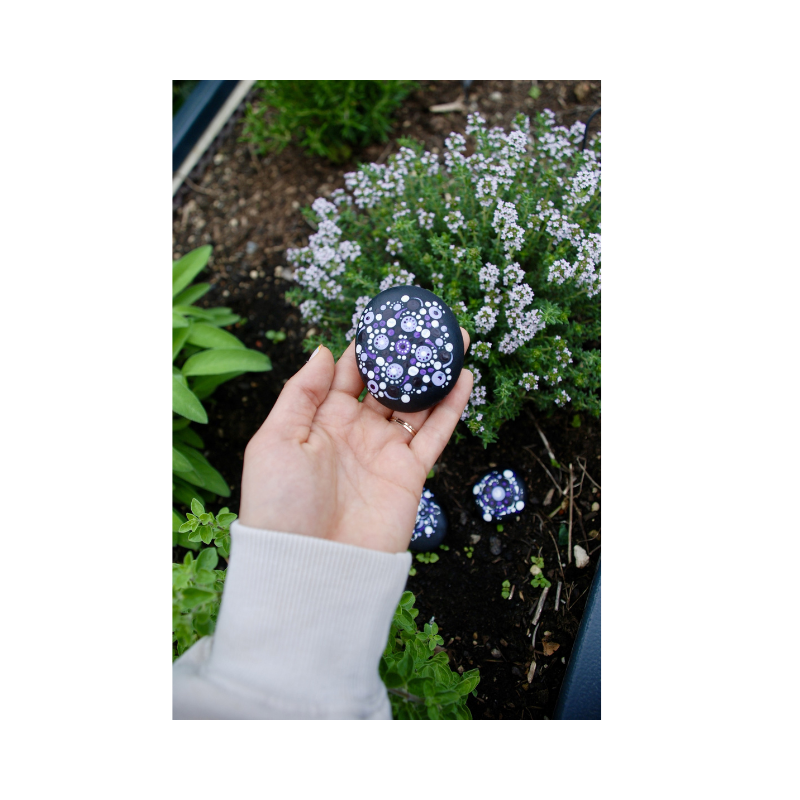 Hand hält handbemalten Dotting-Stein im feministischen Pride-Design, dekorativer Kunststein mit Punktmuster im Garten