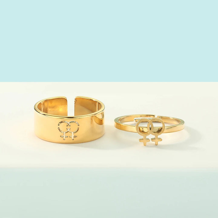 Zweiteiliges goldfarbenes Ring-Set mit verstellbaren Ringen und modernem Symbol-Design auf hellem Hintergrund