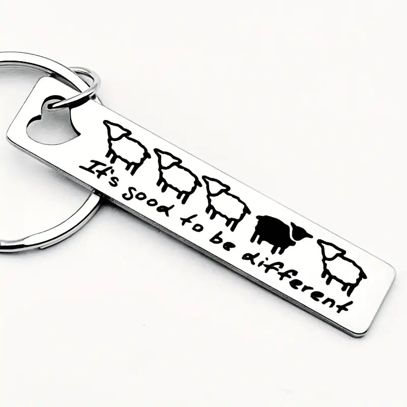 Metall-Schlüsselanhänger mit fünf Schafen, eines schwarz, und Text "It's good to be different" auf weißem Hintergrund