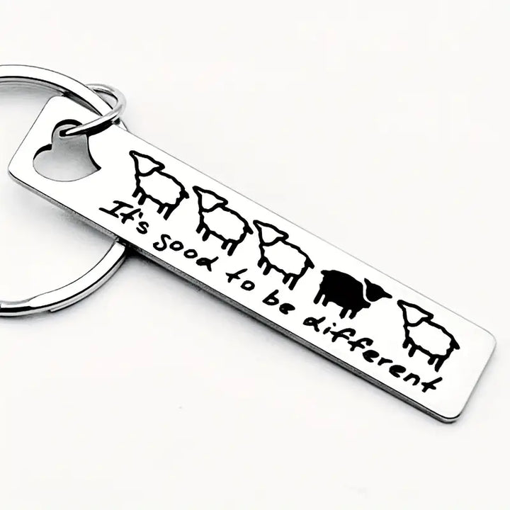 Metall-Schlüsselanhänger mit fünf Schafen, eines schwarz, und Text "It's good to be different" auf weißem Hintergrund