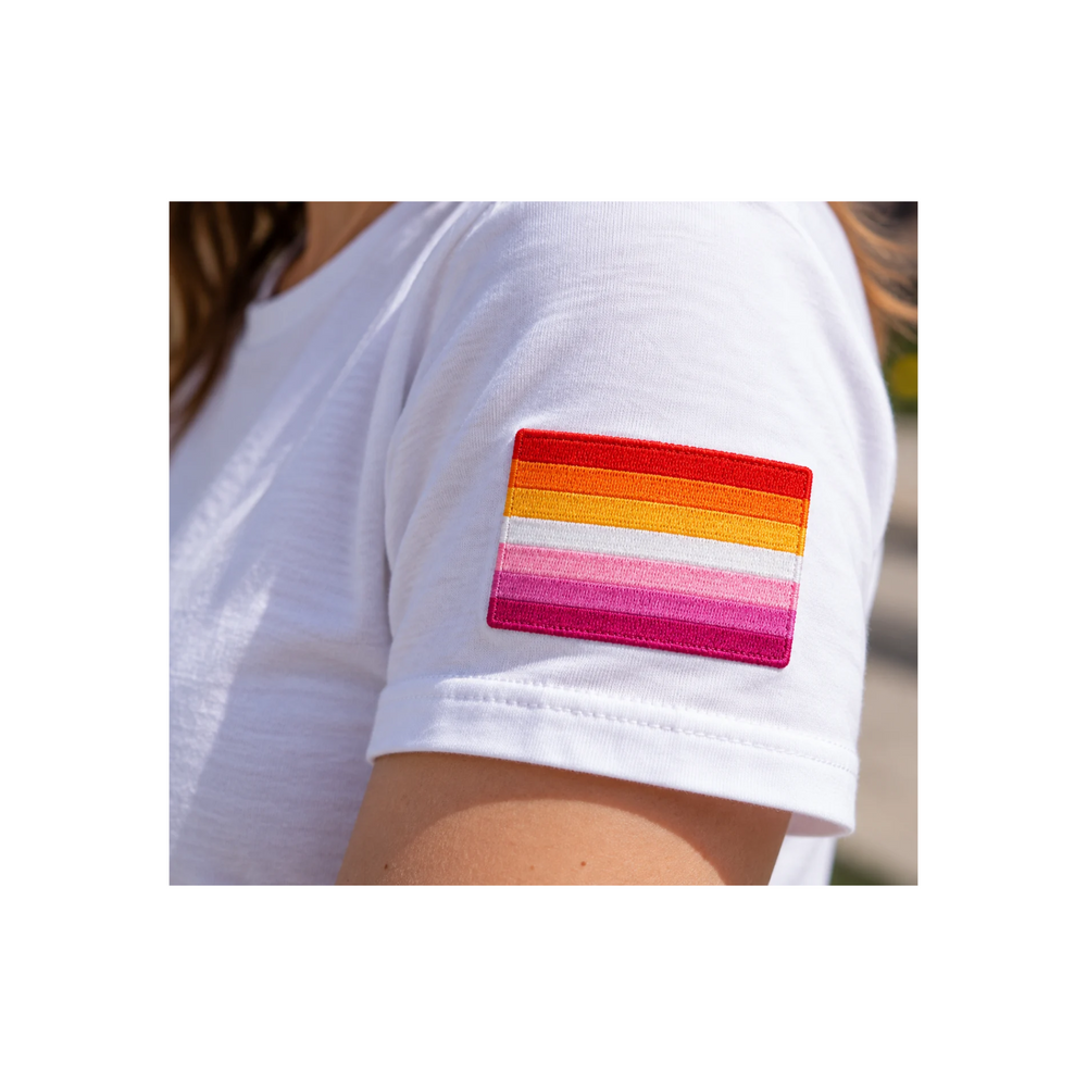 Lesbian Pride Patch mit sieben Streifen der Sunset-Flagge auf dem Ärmel eines weissen T-Shirts. Gestickter lesbischer Aufnäher in Orange-, Weiss- und Rosatönen.
