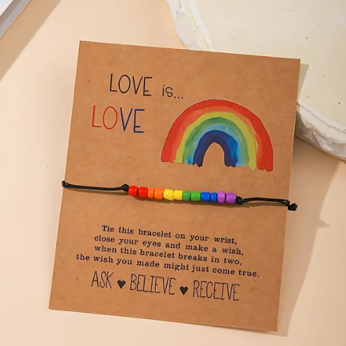 Love-is-Love Armband mit schwarzer Schnur und Regenbogen-Perlen, befestigt auf brauner Kartonkarte mit Regenbogenmotiv