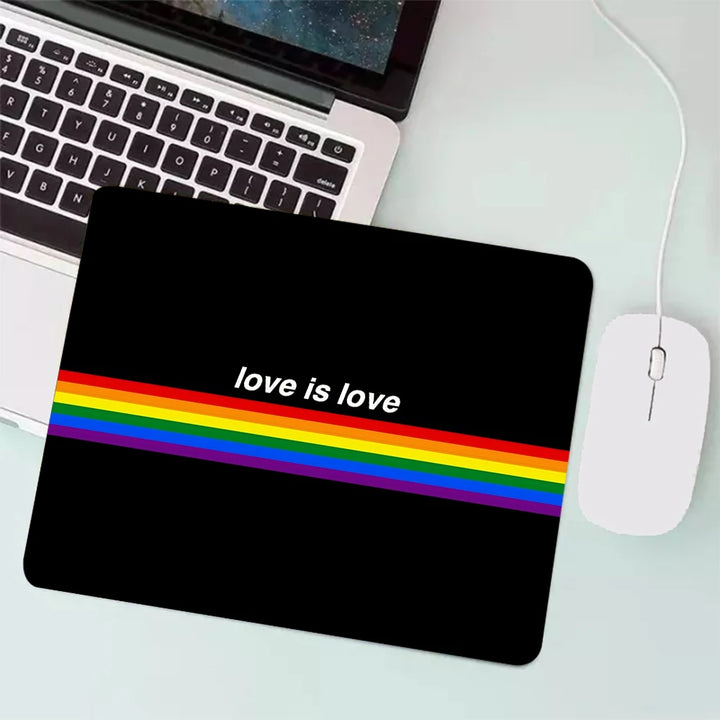 Schwarzes Mauspad mit einem Regenbogenstreifen und dem Schriftzug ‚love is love‘, neben einem Laptop und einer Maus.