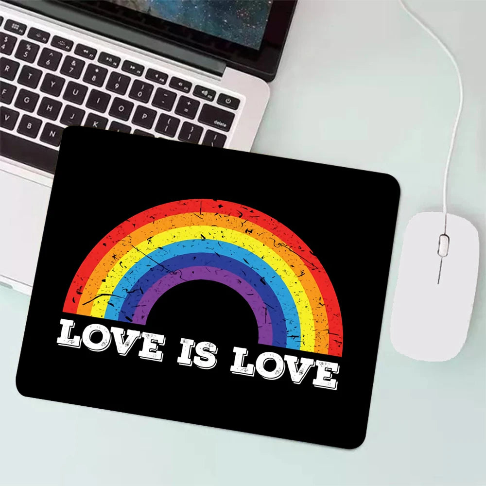 Schwarzes Mauspad mit einem Regenbogen und dem Schriftzug ‚Love is Love‘, platziert neben einem Laptop und einer Maus.