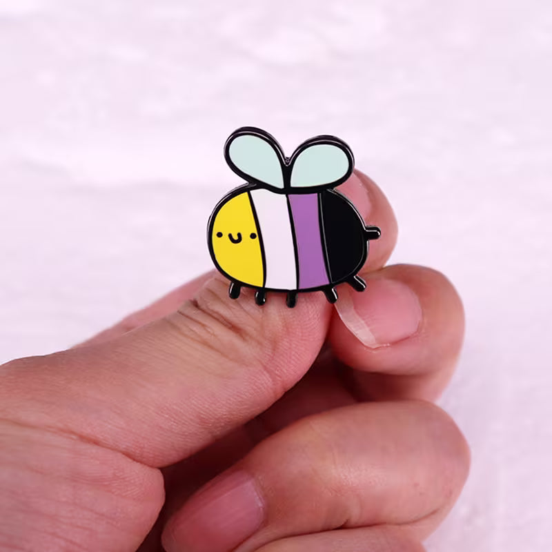 Nonbinary Pride Bienen-Pin in Gelb, Weiss, Violett und Schwarz in der Hand gehalten