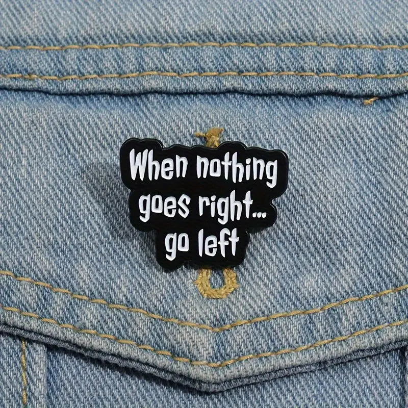 Schwarzer Statement-Pin „When nothing goes right… go left“ an einer blauen Jeansjacke befestigt