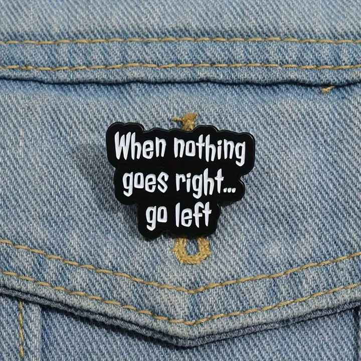Schwarzer Statement-Pin „When nothing goes right… go left“ an einer blauen Jeansjacke befestigt