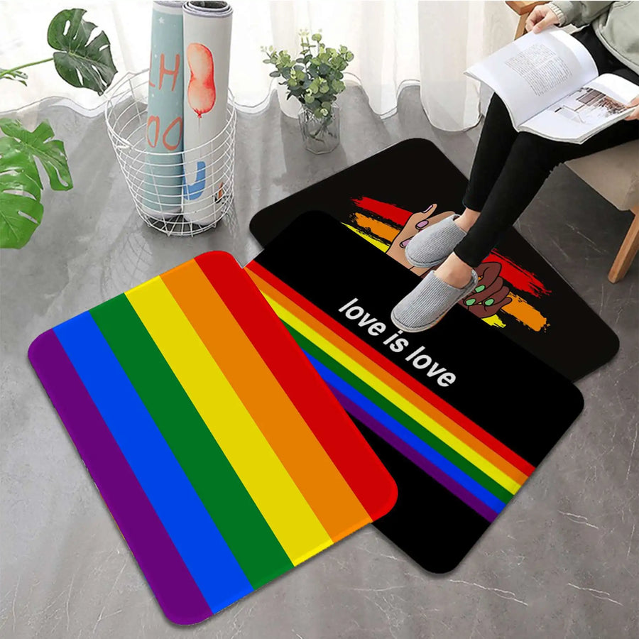 Drei Fußmatten mit Pride-Designs, darunter eine Regenbogenflagge, der Schriftzug ‚Love is Love‘ und Hände in Pride-Farben, in einem modernen Wohnraum.