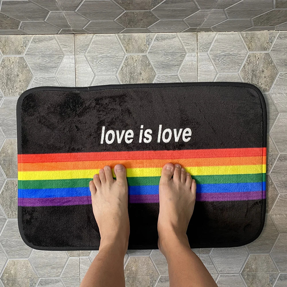 Schwarze Fußmatte aus Polyester mit Regenbogenstreifen und Schriftzug auf Fliesenboden