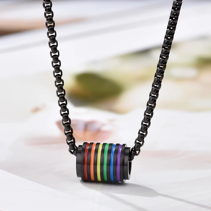 Eine elegante schwarze Halskette mit einem zylindrischen Anhänger, der mit Regenbogenstreifen verziert ist. Die Kette hat ein modernes, minimalistisches Design und symbolisiert LGBTQ+-Pride.