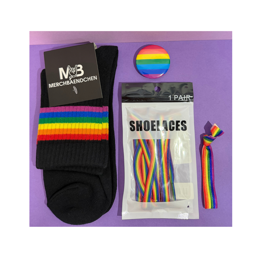 Regenbogen Pride Starter Kit mit schwarzen Socken, Regenbogen-Schnürsenkeln, Armband und Pride-Pin auf violettem Hintergrund.