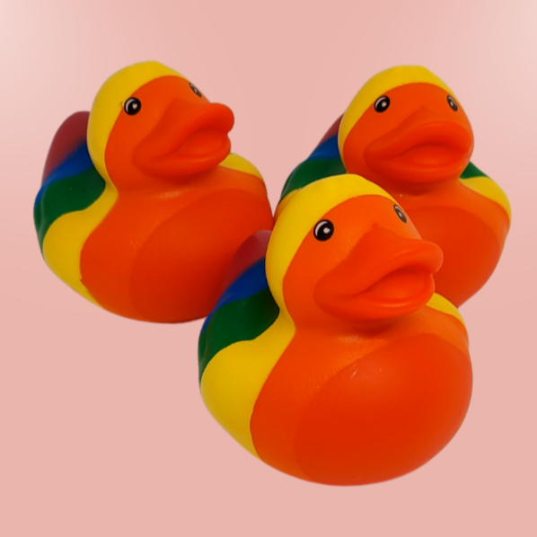 Drei bunte Quietscheentchen mit Regenbogenmuster auf einem rosa Hintergrund.