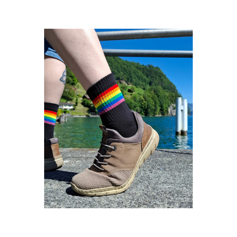 Person trägt schwarze Pride Socken mit Regenbogenstreifen am Seeufer in der Schweiz