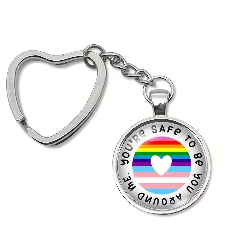 Schlüsselanhänger mit herzförmigem Metallring und rundem Anhänger mit Regenbogenstreifen und weißem Herz in der Mitte; Text auf dem Anhänger: ‘You’re safe to be around me’.