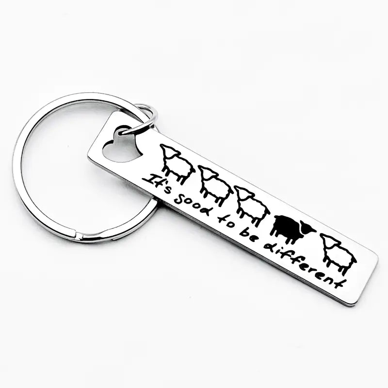 Metall-Schlüsselanhänger „It’s good to be different“ mit fünf Schafen, eines schwarz, auf weißem Hintergrund