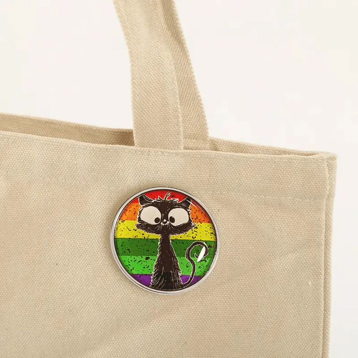 Runder Emaille-Anstecker mit bunter Regenbogenflagge im Hintergrund und einer schwarz gezeichneten, großäugigen Katze im Vordergrund.
