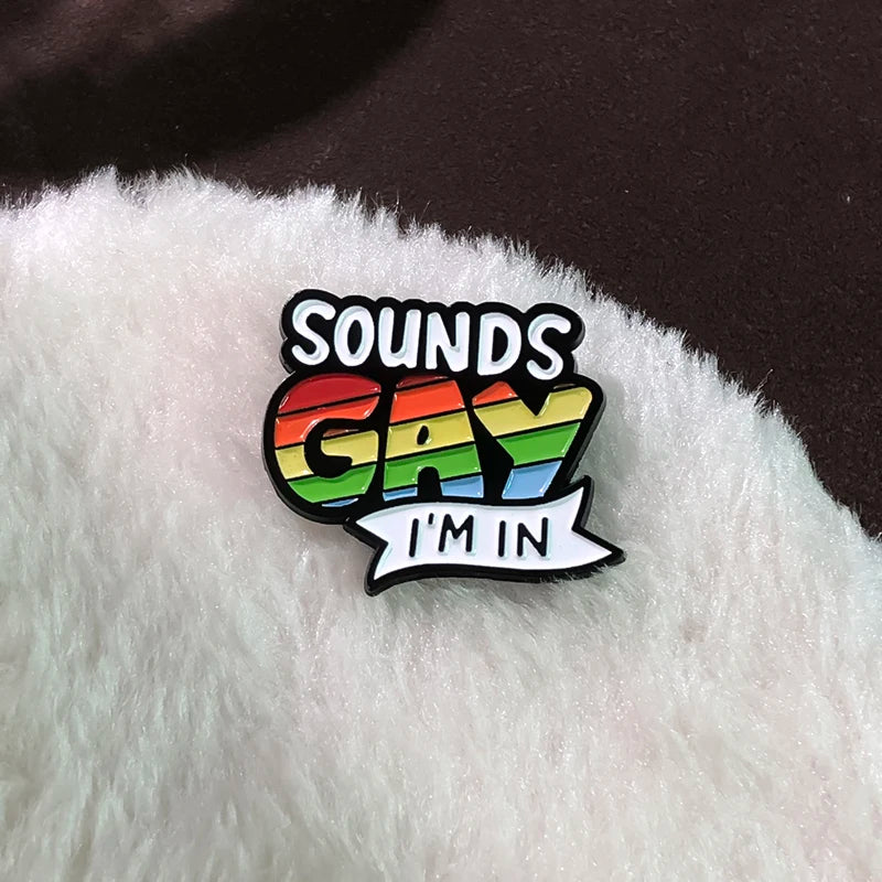 „Sounds Gay I’m In“-Pride-Pin in Regenbogenfarben, befestigt auf weichem, hellem Stoff.
