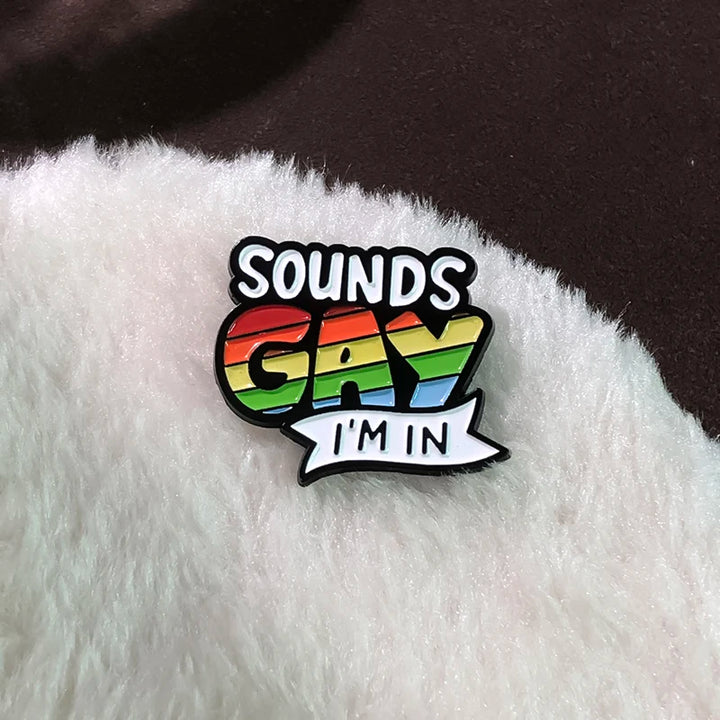 „Sounds Gay I’m In“-Pride-Pin in Regenbogenfarben, befestigt auf weichem, hellem Stoff.

