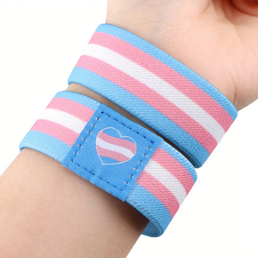 Elastisches Armband in den Farben der Transgender-Flagge (hellblau, rosa, weiß) mit Herzsymbol – getragen am Handgelenk.